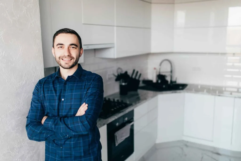 Smiling man standing in a modern kitchen with folded arms, representing real estate confidence and the decision to.