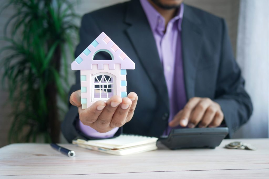 Businessman holding a small model house while using a calculator, representing real estate valuation and the steps people take when they want to.